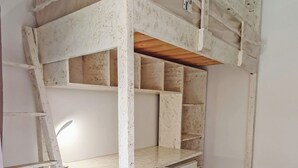 Una cama litera con escalera, estantes de madera y un pequeño conjunto de cajones.
