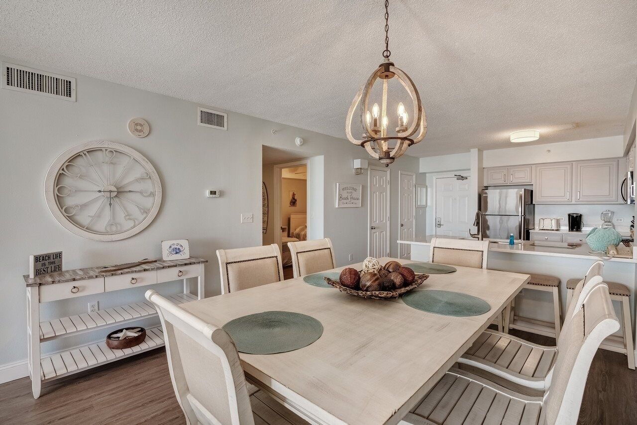 A dining area with a wooden table, chairs, a chandelier, and a wall clock.