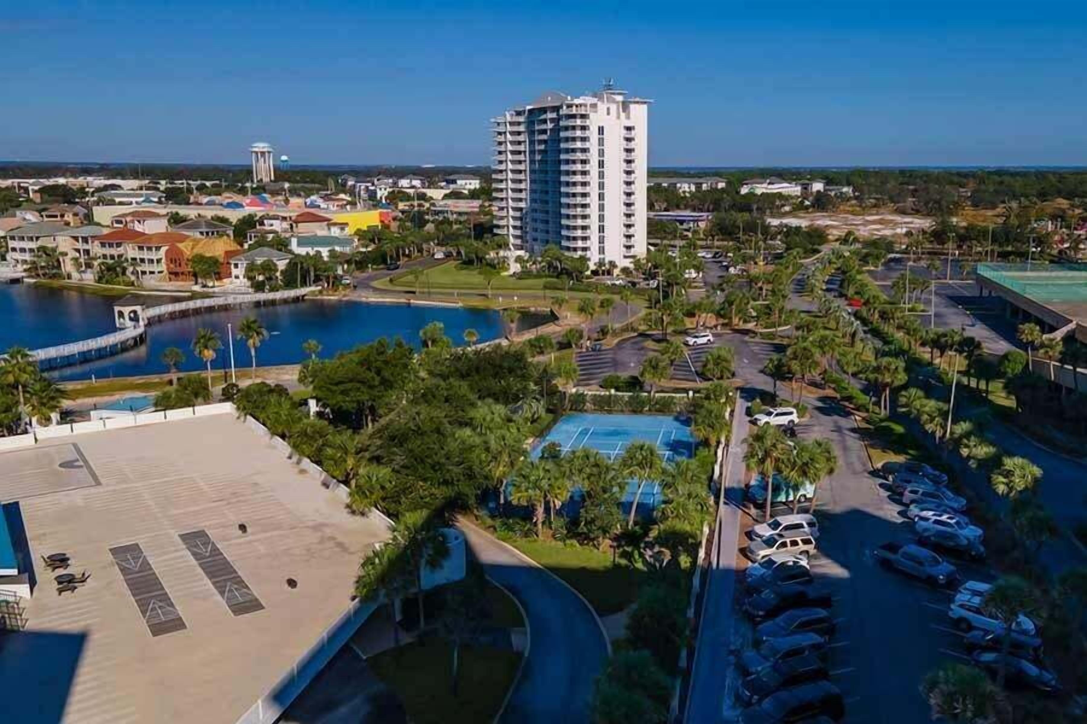 A high-rise hotel with a pool, parking area, and surrounding greenery.