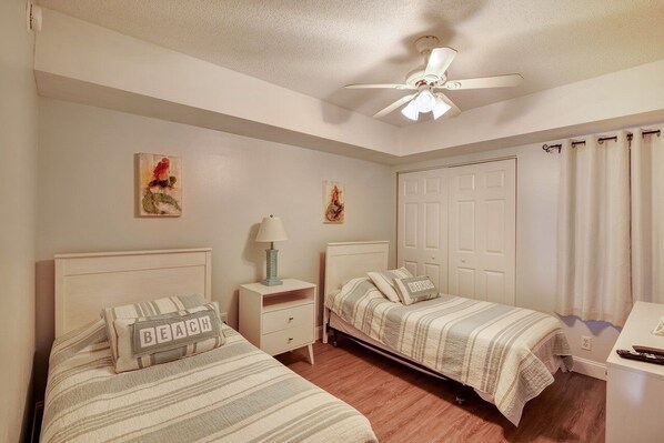 Une chambre avec deux lits, un ventilateur de plafond et une porte.