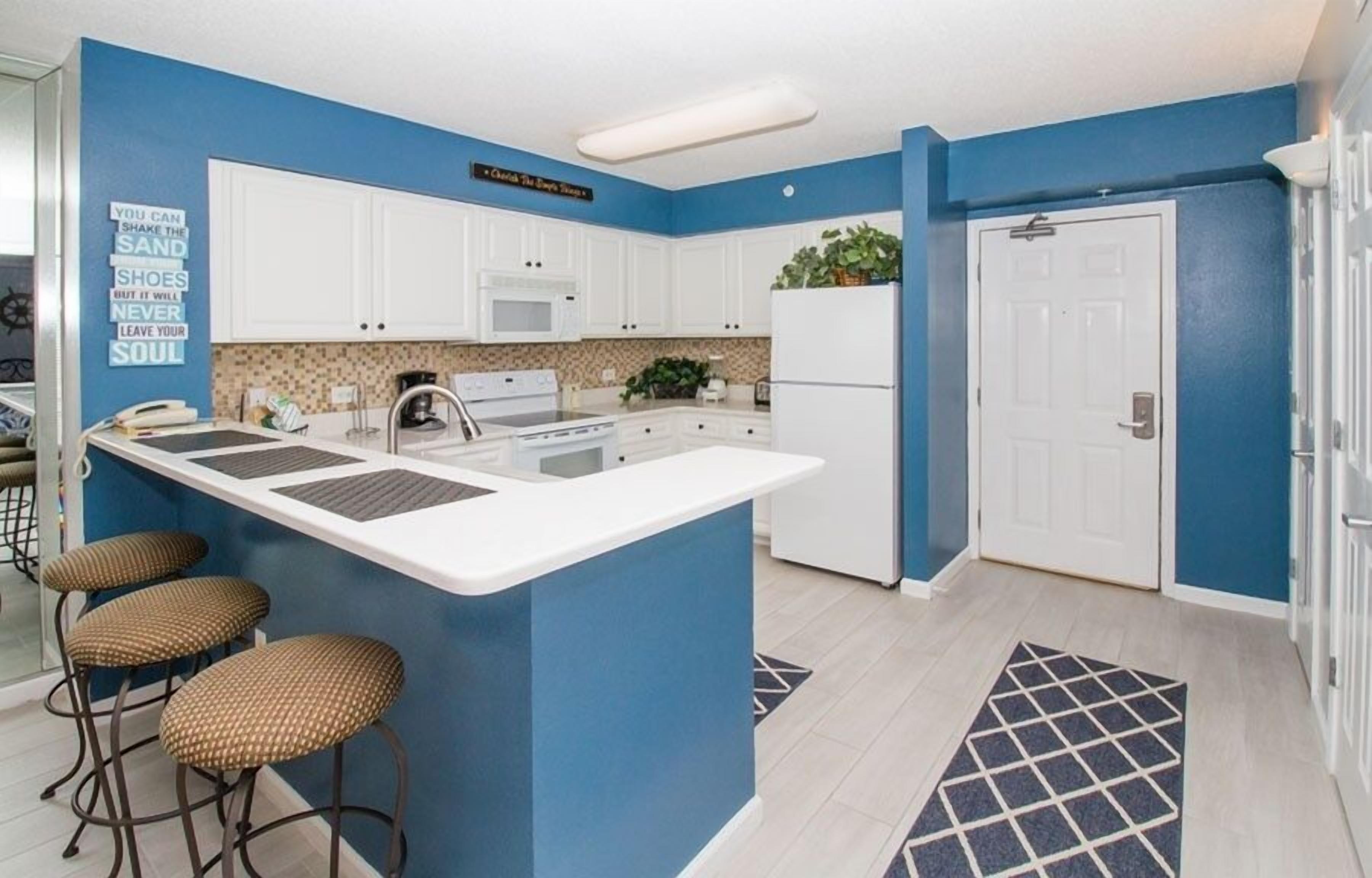 Una cocina moderna con una isla central, armarios blancos y una pared de acento azul.