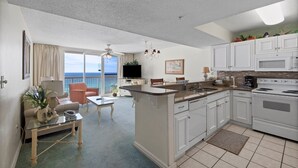 A modern kitchen with white cabinets, a central island, and a view of the ocean. - Pelican Beach 1008 1 Bedroom Condo by Pelican Beach Management (Destin)