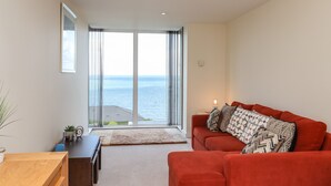 Un salón moderno con un sofá rojo, una mesa de centro de madera y vistas al mar a través de amplias ventanas.