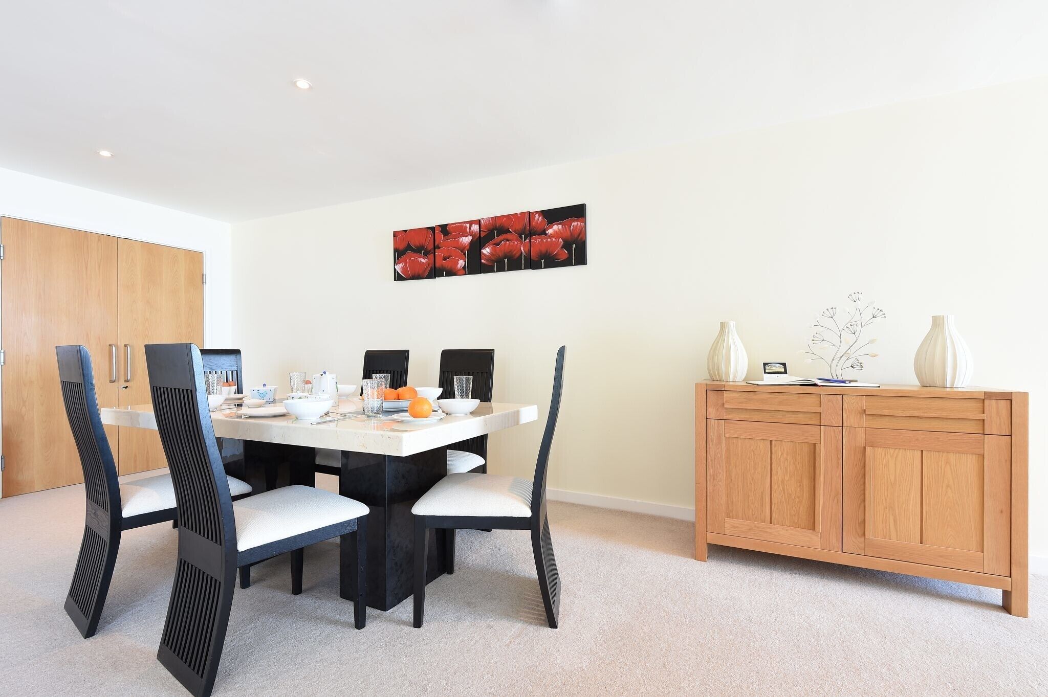 A dining area with a white table, black chairs, and a wooden cabinet with decorative items.