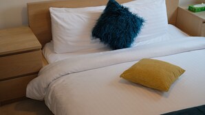 Een net opgemaakt bed met witte lakens, een zacht blauw kussen en een mosterdgeel kussen.