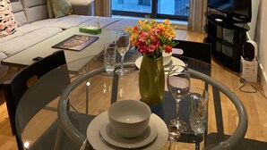 Een moderne woonkamer met een bank, een eettafel gedekt met borden, glazen en een bloevas. Een televisie is aan de muur bevestigd en een raam biedt uitzicht op de stadszicht.