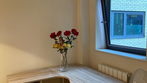 Een hoekkamer met een ingebouwd bureau, een radiator, een raam met zonwering en een vaas met bloemen.