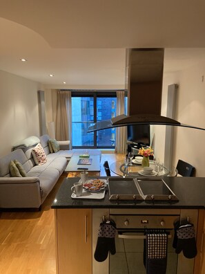 Eine moderne Küche mit Kochinsel, ein Essbereich mit Glastisch und ein Wohnzimmer mit Sofa.