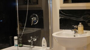 Een badkamer met een douche met glazen wand, een witte wastafel en een spiegel boven de wastafel.