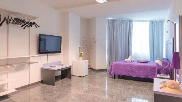 A modern hotel room with a bed, a desk, a television, and a bathroom area. - Delta rooms (Olbia)
