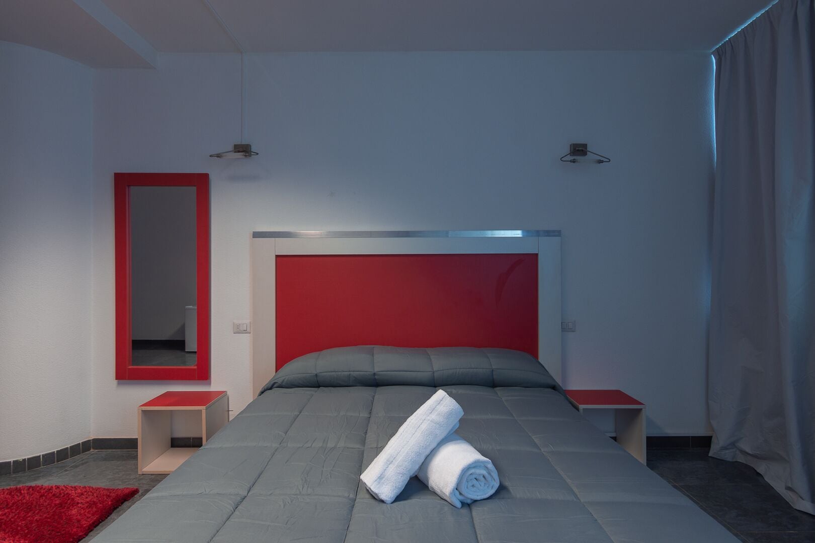 Una camera da letto moderna con una testiera rossa, un letto grande, due comodini, uno specchio e un tappeto rosso.