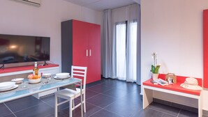 A modern living room with a dining area, a flat-screen TV, a red cabinet, and a large window with curtains. - Delta rooms (Olbia)