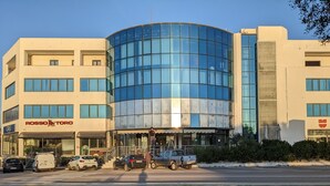 A modern building with a curved glass facade, a visible entrance, and signage for 'ROSSOTORO' and 'WÜRTH'. - Delta rooms (Olbia)