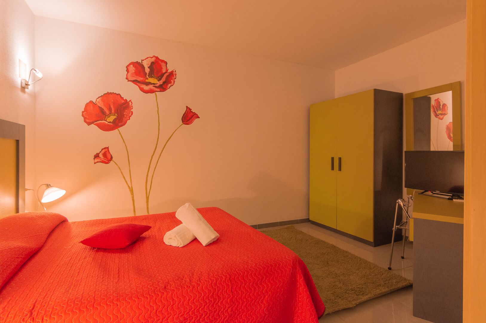A hotel room with a bed, a yellow wardrobe, a mirror, and a massage table.