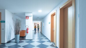 A hotel corridor with checkered flooring, a fire extinguisher, and doors marked with room numbers. - Delta rooms (Olbia)