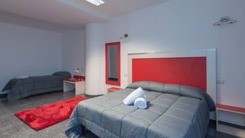 A modern hotel room with a large bed, a smaller bed, a red accent wall, and a red rug.