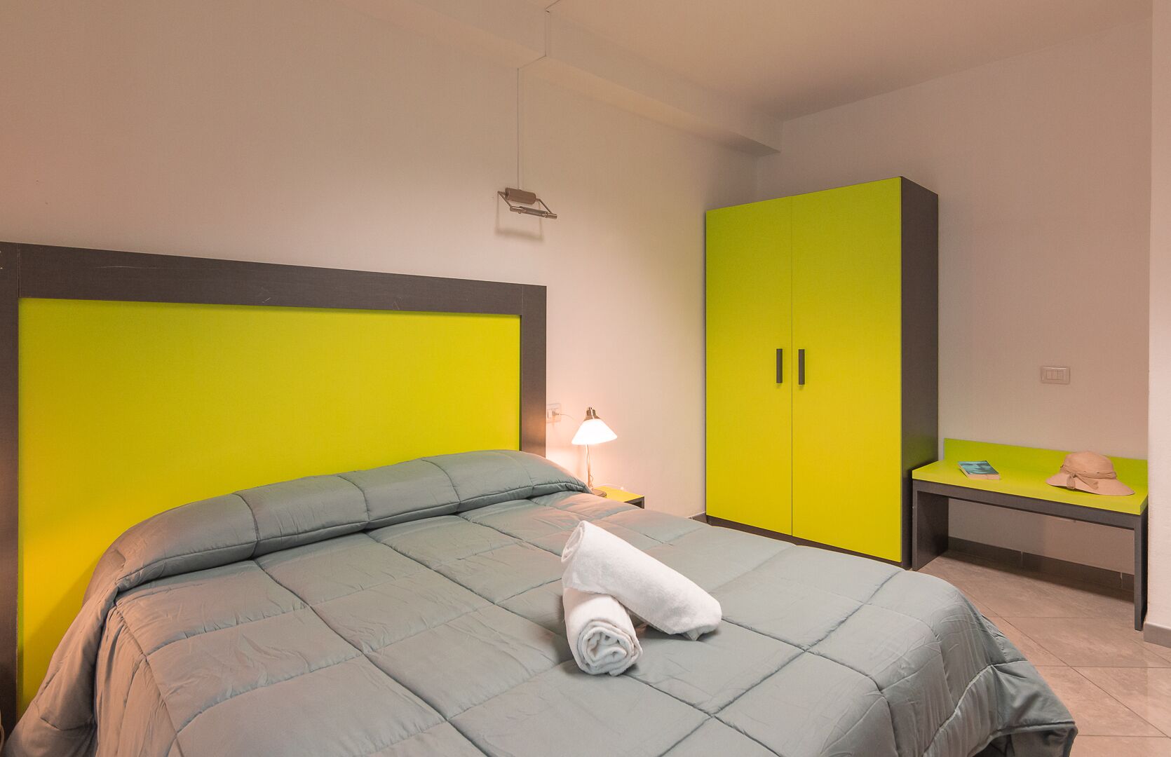 Ein Bett mit grauem Kopfteil und einem gelben Kleiderschrank.