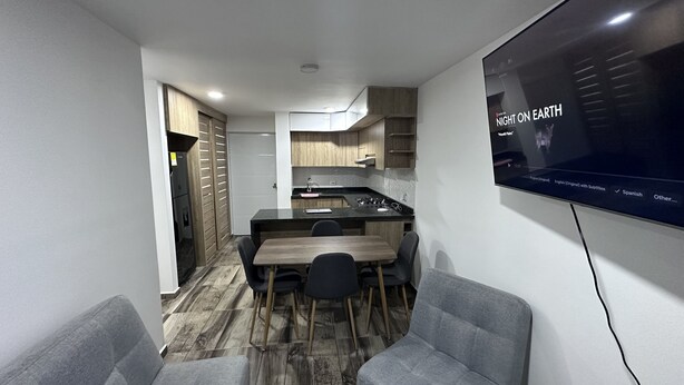 Een compacte keuken met een eethoek, een flatscreen televisie aan de muur en een zithoek met een bank en stoelen.