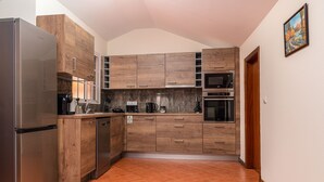 A compact kitchen with wooden cabinets, a stainless steel refrigerator, a microwave, and a dishwasher. - Sunset House (Arco da Calheta)