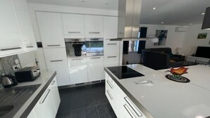Una cocina moderna con armarios blancos, una isla central y un comedor con sofá negro.