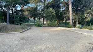Un espacio al aire libre cercado, con suelo de grava, rodeado de árboles y vegetación.