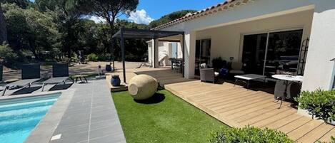 Un jardin avec une piscine, une terrasse en bois et un espace patio aménagé avec du mobilier d’extérieur.