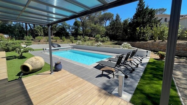 Un espacio al aire libre techado con piscina, terraza de madera y mobiliario exterior.