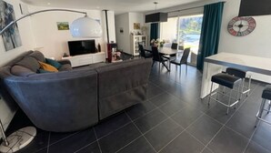 Una sala de estar moderna con sofá, comedor con mesa y sillas, televisor y un ventanal con cortinas.