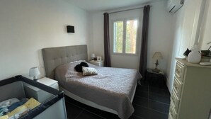 Un dormitorio con cama, mesitas de noche, cómoda, ventana con cortinas y equipo de aire acondicionado.