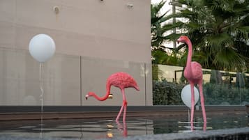 A pink flamingo statue in a water feature with a white balloon and a building in the background.