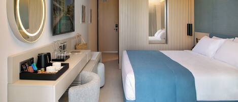 A modern hotel room with a large bed, a desk with a coffee maker, a chair, and a large mirror.