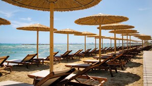 Une plage bordée de rangées de chaises longues en bois et d’ombrelles en chaume.