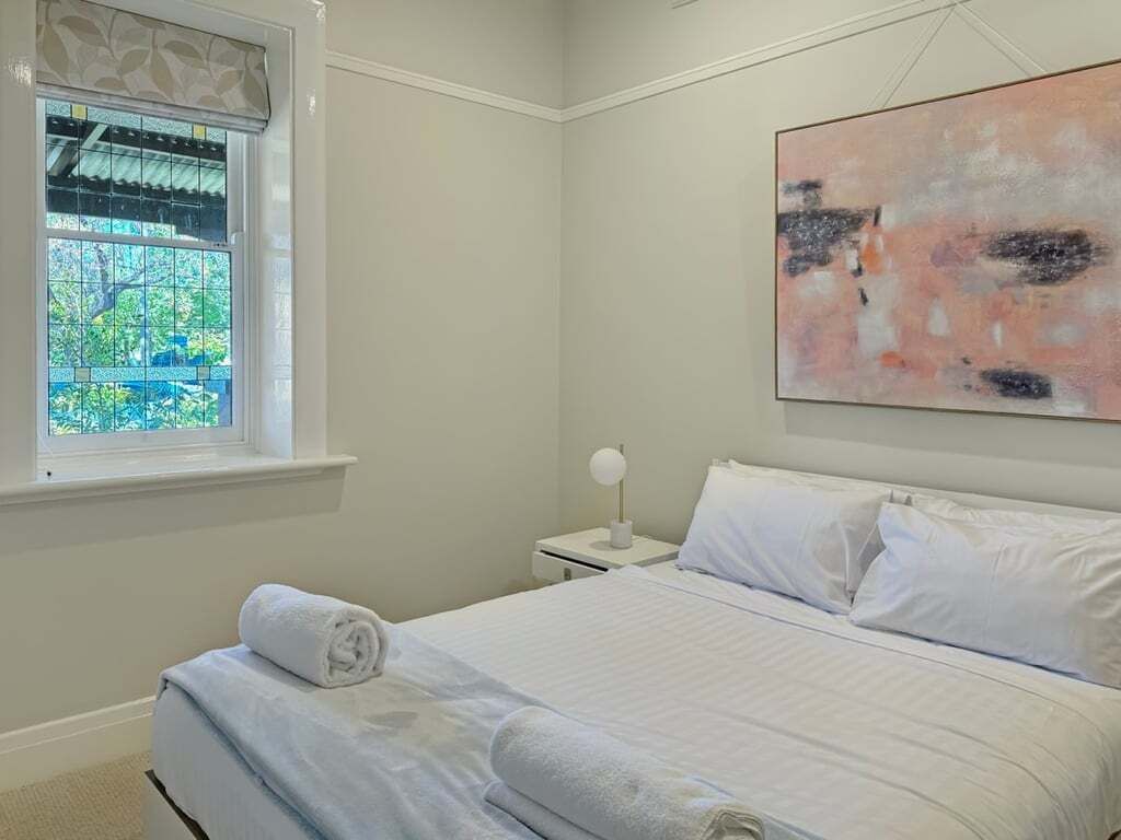 Een slaapkamer met een bed, een nachtkastje, een raam met uitzicht en een schilderij aan de muur.