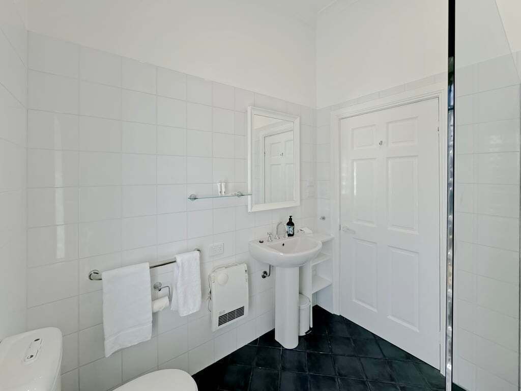 Un bany amb rajoles blanques, un lavabo blanc, un vàter i una porta.