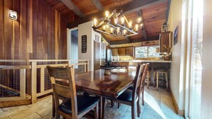 A wooden interior with a dining table and chairs, a kitchen area, and a view of the outdoors. - Mammoth Estates #140 2 Bedroom Condo by RedAwning (Mammoth Lakes)