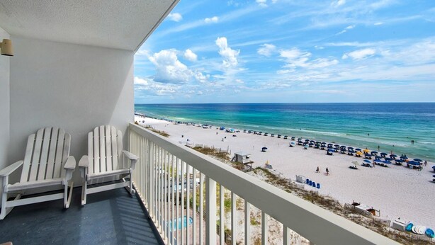 A balcony with two white Adirondack chairs, overlooking a beach with umbrellas and people. - Pelican Beach 0708 1 Bedroom Condo by Pelican Beach Management (Destin)