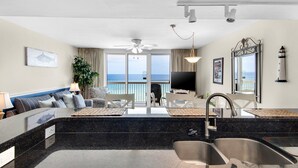 A modern hotel room with a kitchen area, a dining table, a sofa, and a TV. - Pelican Beach 0708 1 Bedroom Condo by Pelican Beach Management (Destin)
