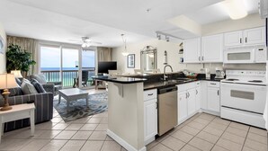 A modern kitchen with white cabinets, a central island, and a dining area with a view of the ocean. - Pelican Beach 0708 1 Bedroom Condo by Pelican Beach Management (Destin)