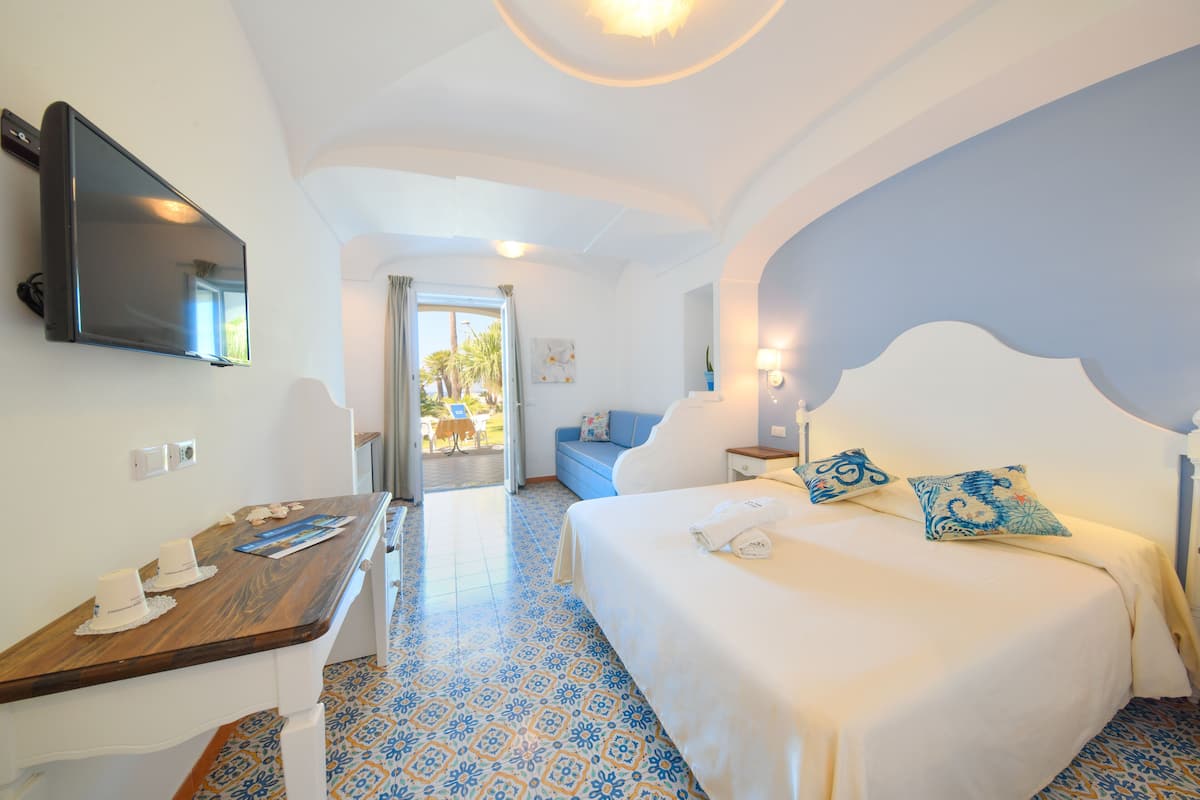A hotel room with a bed, a desk, a TV, and a view of the outside.