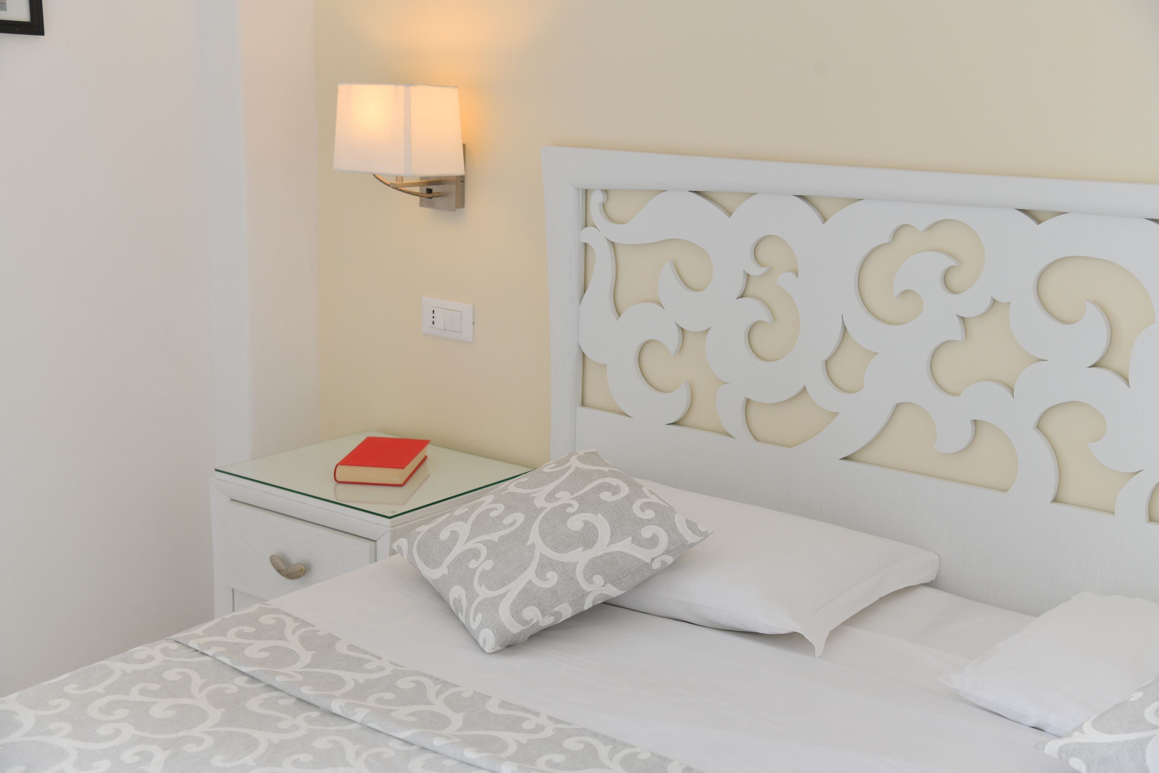 A neatly made bed with patterned bedding, a bedside table with a book, and a wall-mounted lamp.