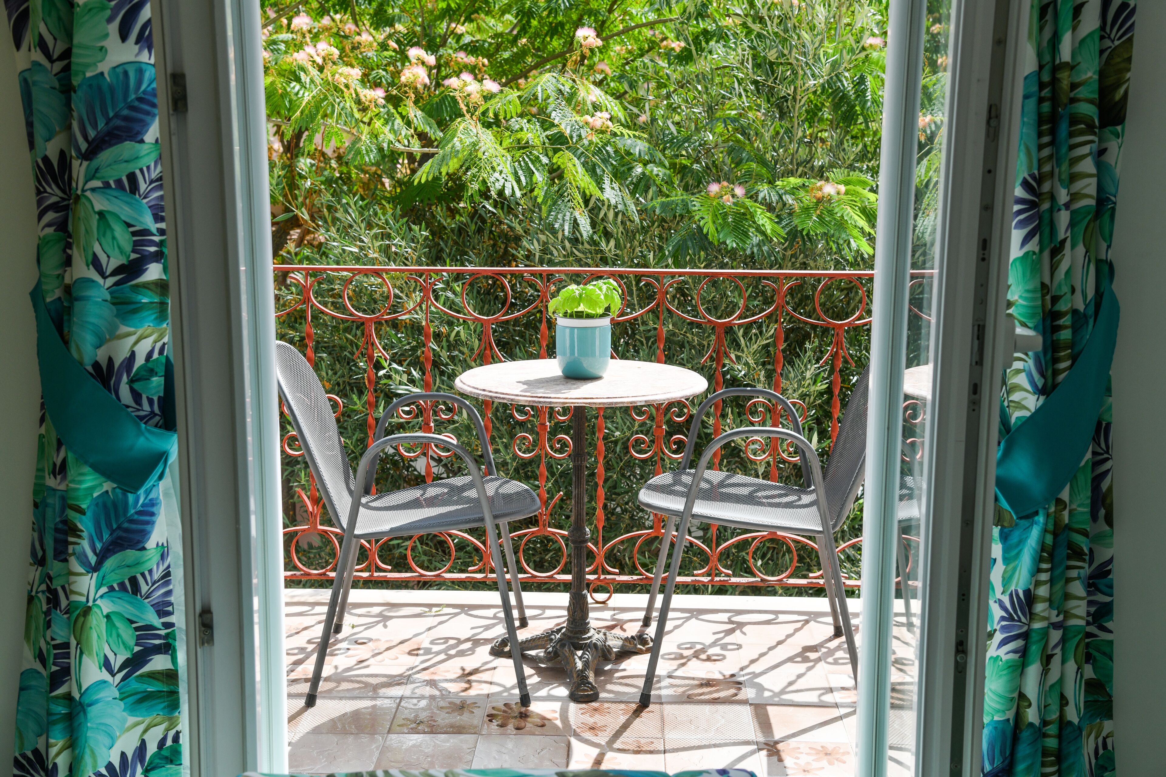 A balcony with a round table and two chairs, a potted plant, and a metal railing.