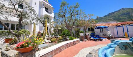 A hotel with a clear view of the pool area, including a small fountain and lounge chairs.