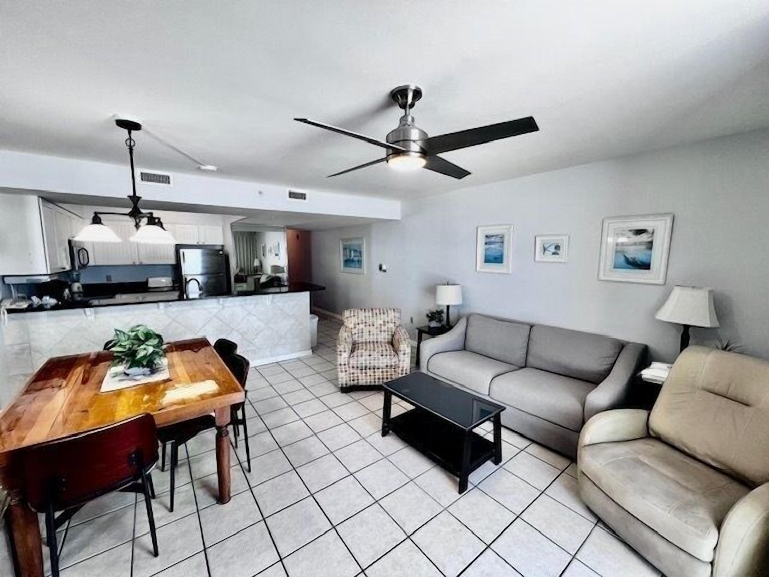 A modern living room with a dining area, a sofa, a coffee table, and a ceiling fan.