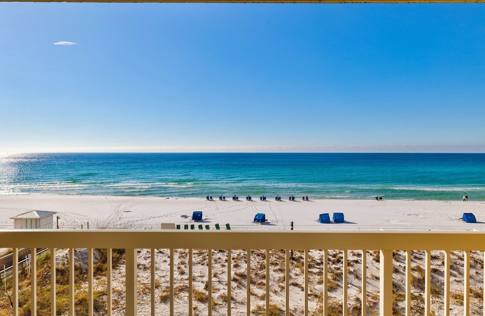 Uitzicht op een strand vanaf een balkon met een hekwerk, zandstrand en oceaan.