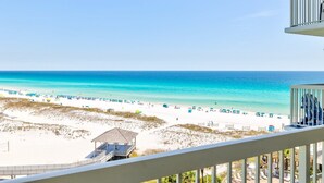 A beach view with a white railing, beach umbrellas, and a small structure on the sand. - Pelican Beach 0815 2 Bedroom Condo by Pelican Beach Management (Destin)