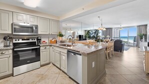 A modern kitchen with a central island, stainless steel appliances, and a dining area with a view. - Pelican Beach 0815 2 Bedroom Condo by Pelican Beach Management (Destin)