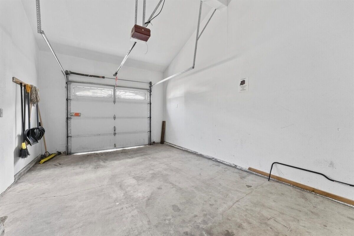 Un garage propre et vide, avec un sol en béton, une porte de garage fermée et un luminaire fixé au plafond.