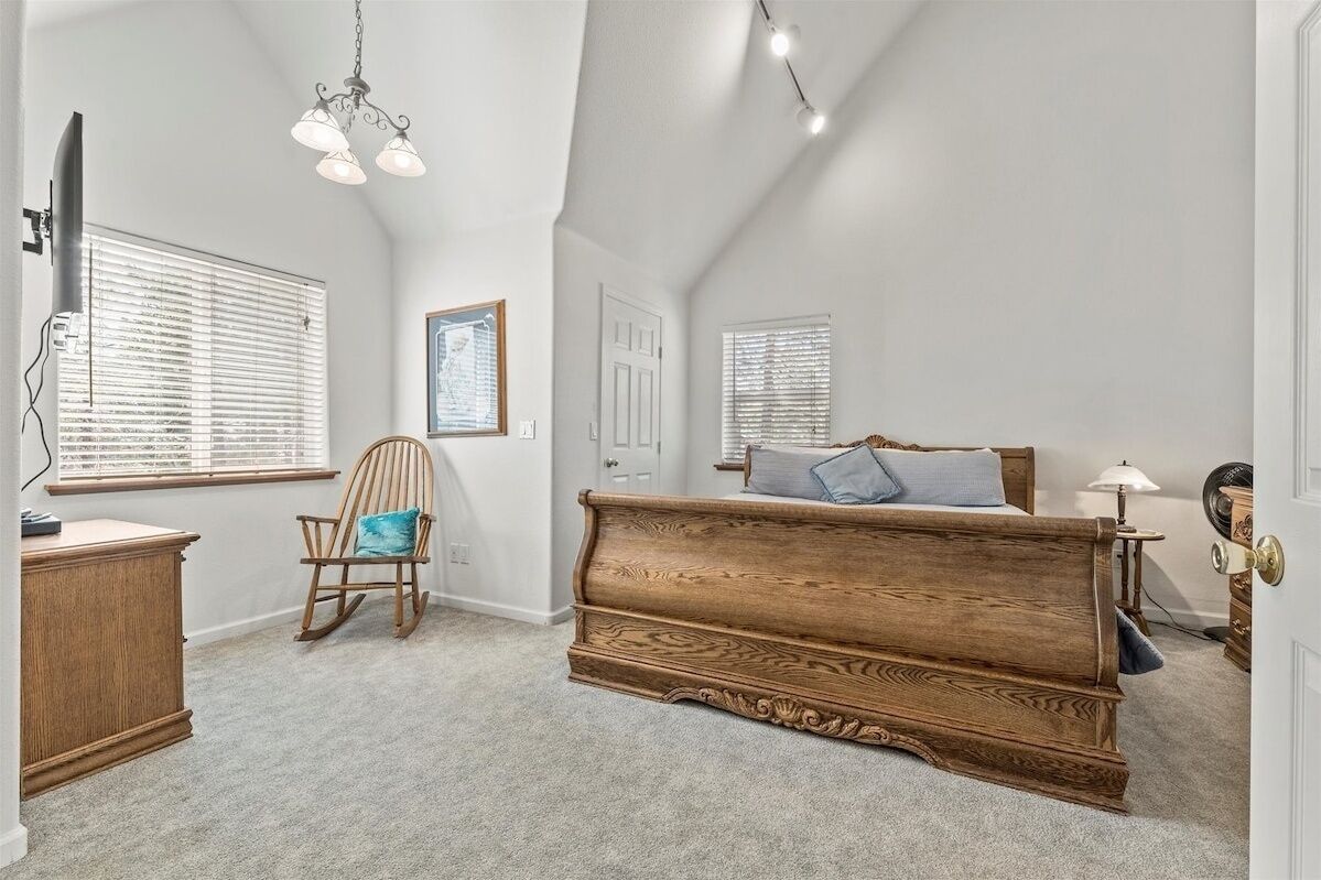 A bedroom with a wooden bed, a rocking chair, a desk, and a window with blinds.