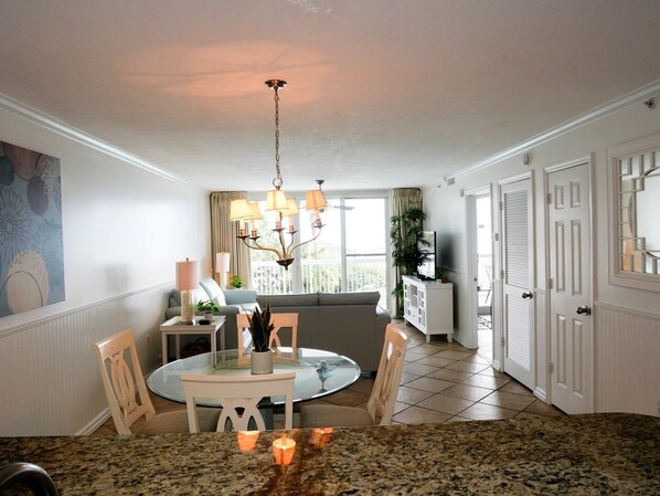 A dining area with a round table, chairs, a chandelier, and a view of the outdoors. - Pelican Beach 0212 2 Bedroom Condo by Pelican Beach Management (Destin)