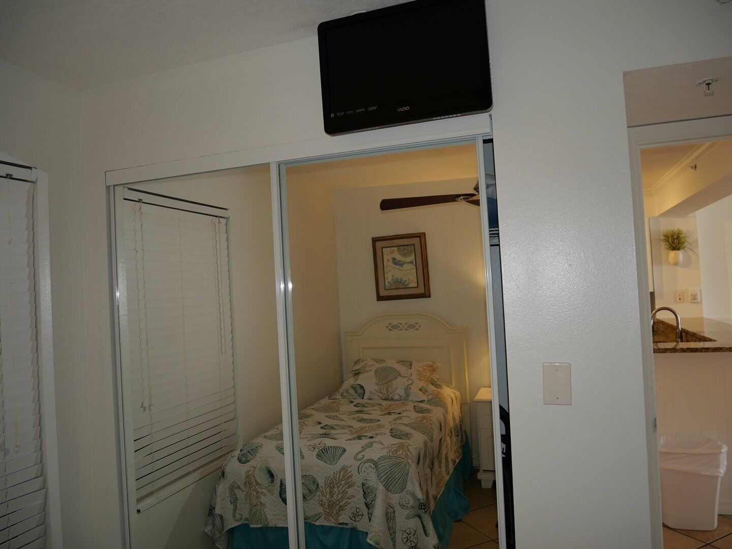 Une chambre à coucher avec un lit, un téléviseur fixé au mur et une fenêtre avec des stores.
